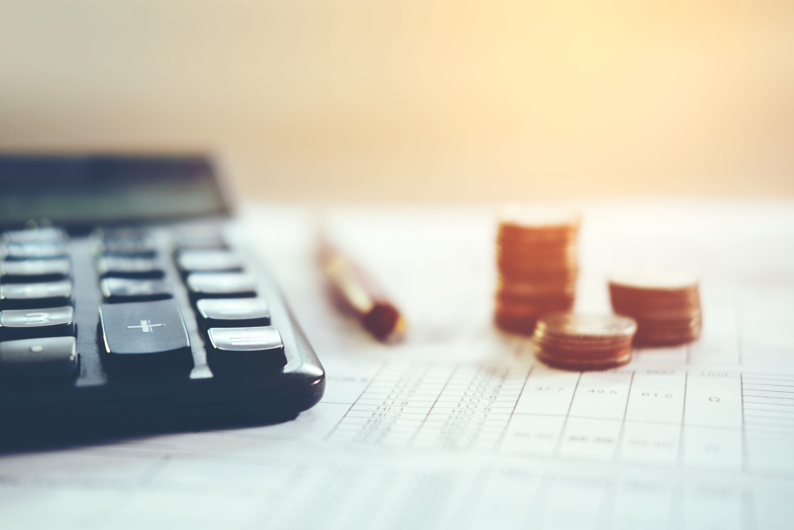 Close-Up Of Document With Calculator And Pen By Coins On Office Desk