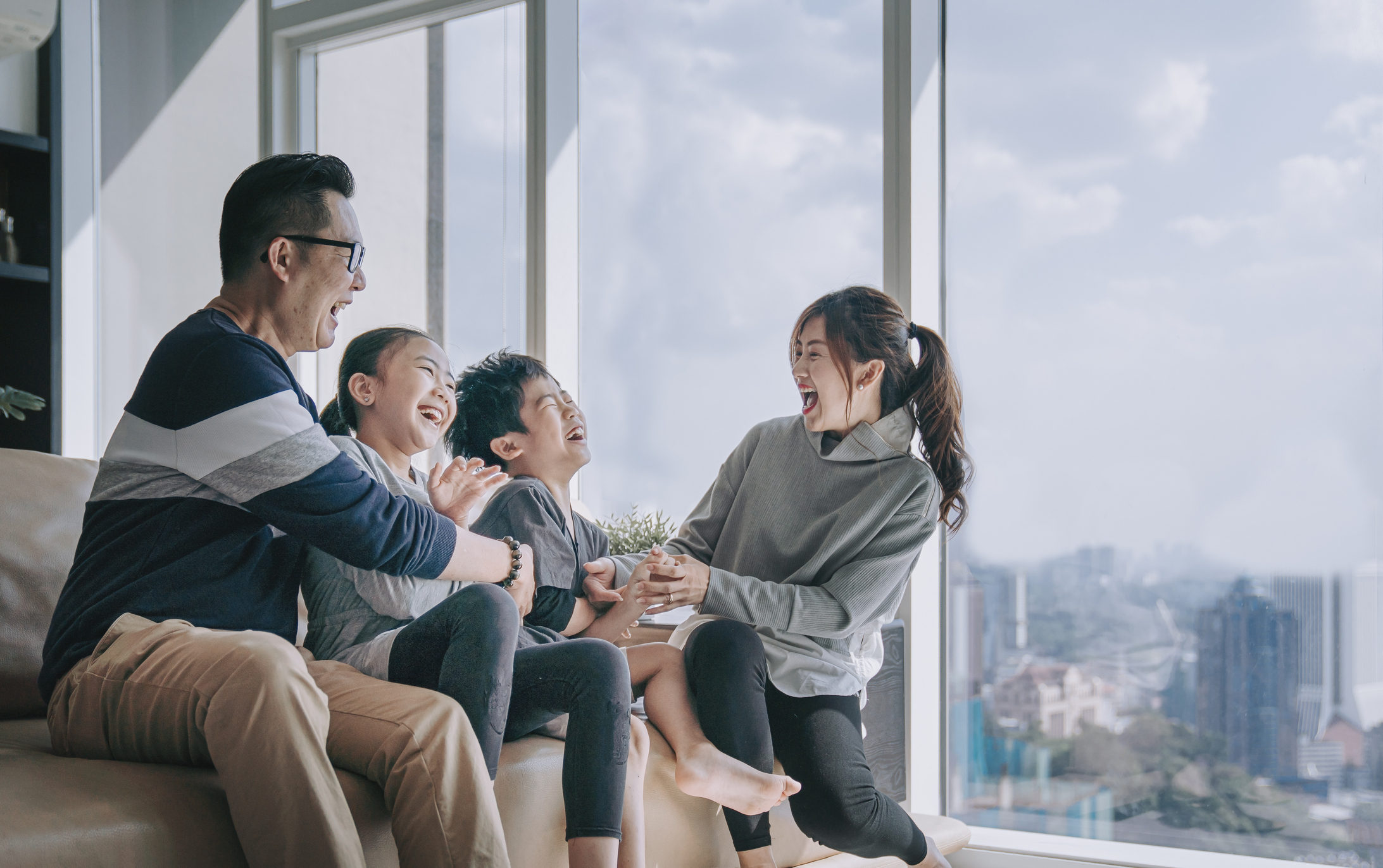 asian chinese 2 parent tickling playing with their children at home in living room cuddle on sofa