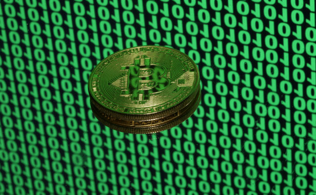 Bitcoin token is seen placed on a monitor that displays binary digits in this illustration picture
