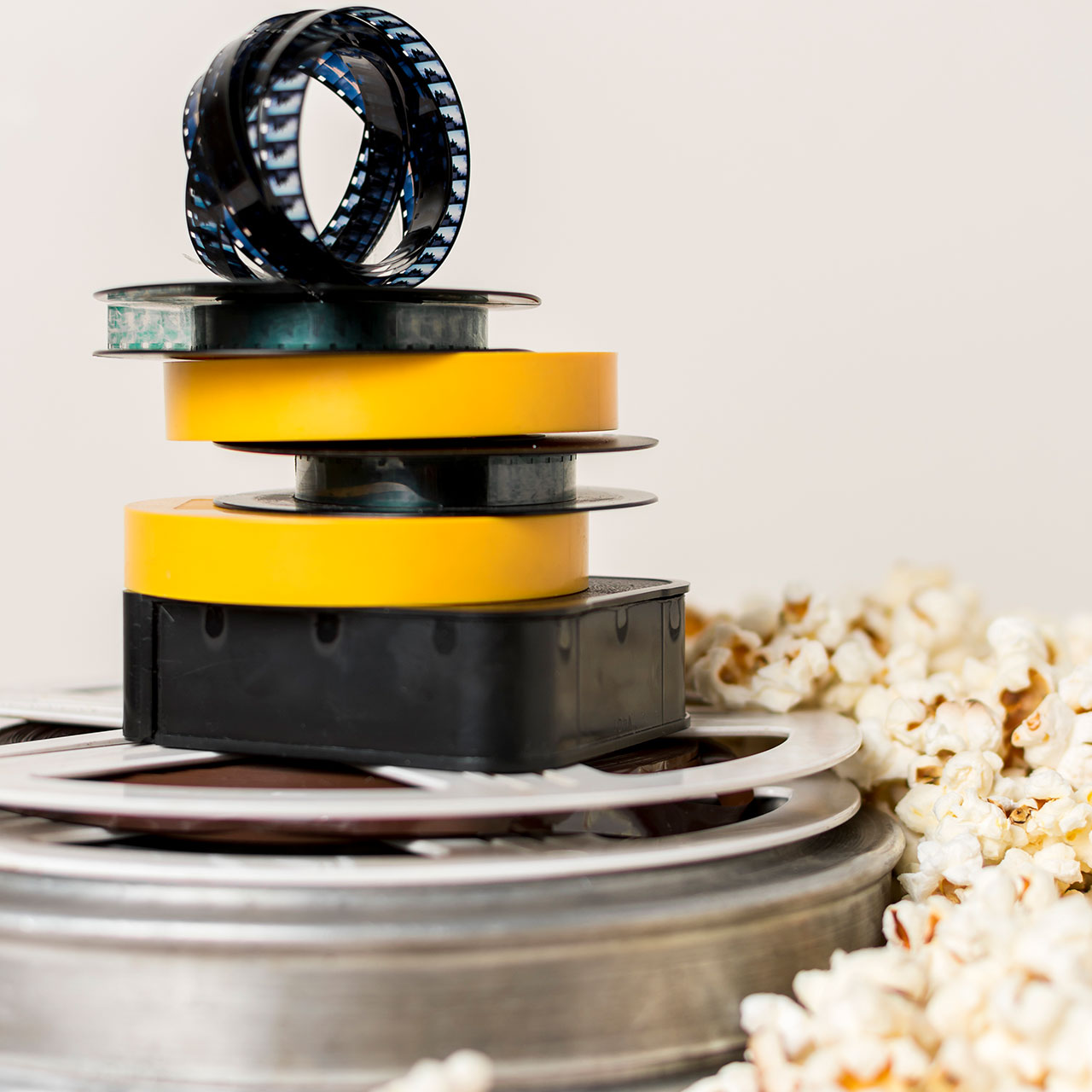stacked-film-reels-with-film-strip-near-popcorn-against-white-background