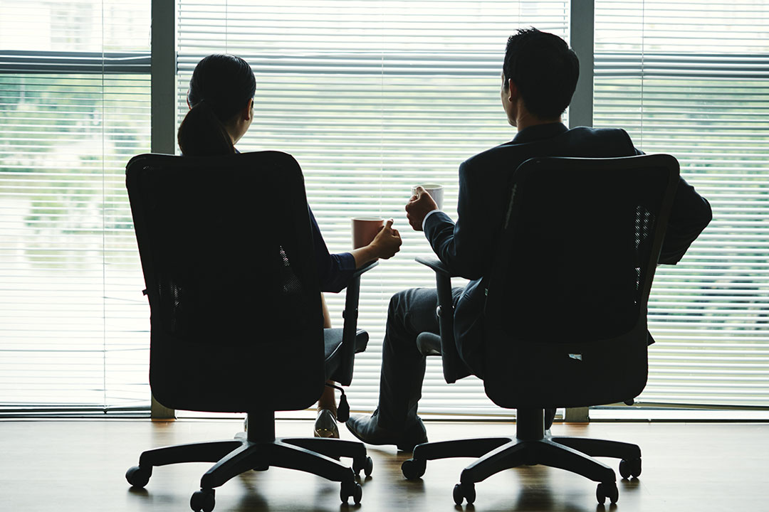 dark-silhouettes-man-woman-sitting-with-mugs-office-chairs-front-window