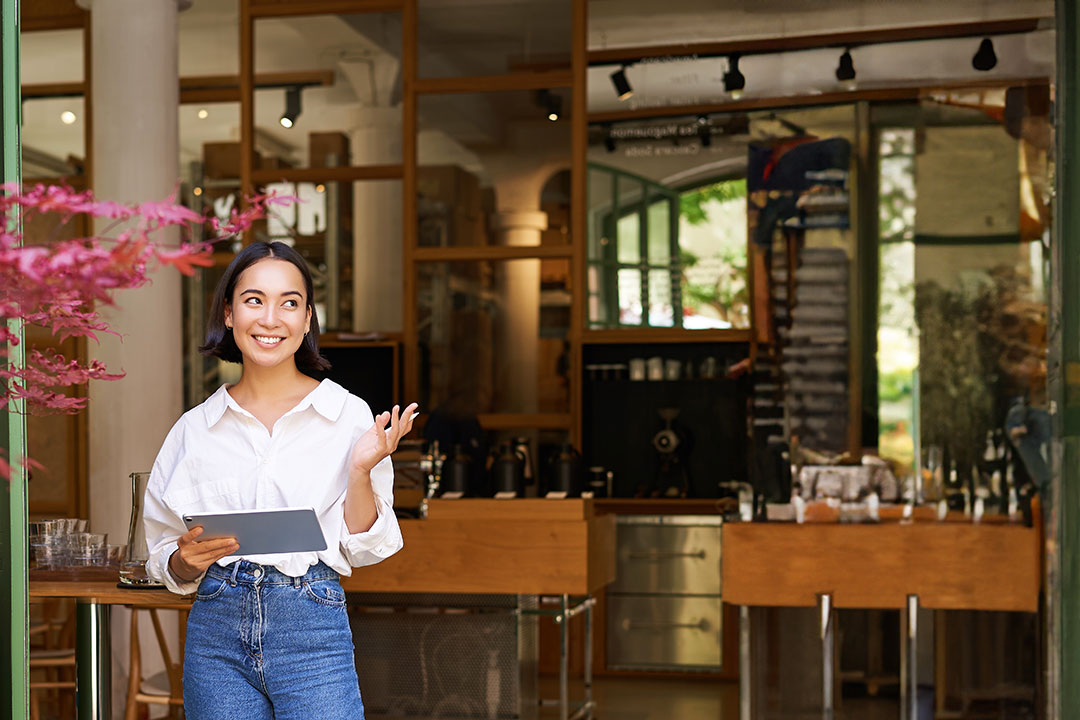 vertical-shot-smiling-asian-businesswoman-waitress-standing-front-cafe-entrance-inviting